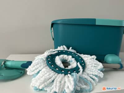 De afbeelding toont een blauwgroen en witte dweilset, inclusief een emmer en een dweil met een ronde, afneembare microvezelkop. De emmer heeft een blauwgroen accent op het handvat. Rechtsonder staat een klein logo met een oranje en blauw ontwerp en de tekst "keurio.nl".