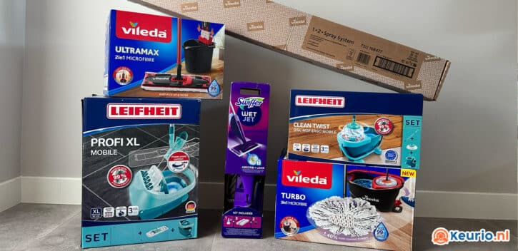 Tegen een muur staan vier verschillende dozen met schoonmaakproducten opgesteld. De merken zijn onder meer Leifheit, Vileda en Swiffer. Getoonde producten zijn diverse dweilsets en een spuitmop voor moeiteloos dweilen. Rechtsonder is het logo van Keurio.nl zichtbaar. Daarnaast is er een lange kartonnen doos aanwezig.